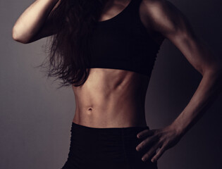 Fototapeta na wymiar Sport muscular woman posing in black sport clothing showing the muscle strong abs, shoulders and arms standing on dark shadow studio background. Front body view Sporty lifestyle.
