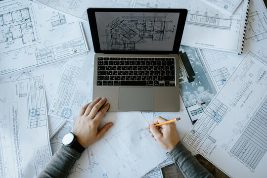 An arhitect working in his office, on his laptop and using a pen, designing a new project.