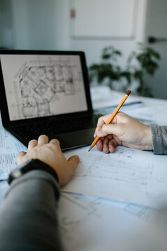 An arhitect working in his office, on his laptop and using a pen, designing a new project.