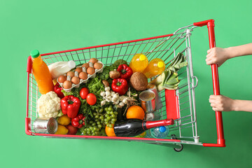 Woman pushing shopping cart full of different food on green background