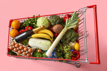 Shopping cart full of food on pink background