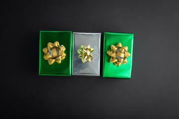 Creative handmade christmas green and silver paper gift boxes with decor on black background, top view.