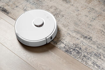 Smart robot vacuum cleaner on the carpet and on the laminate removes dust. - obrazy, fototapety, plakaty