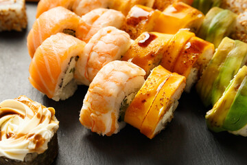 Set of colorful rolls with shrimp, salmon, avocado, cheese on a black stone plate, close-up.