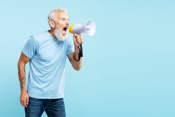Angry mature gray haired man holding loudspeaker shouting something, wearing casual blue t shirt
