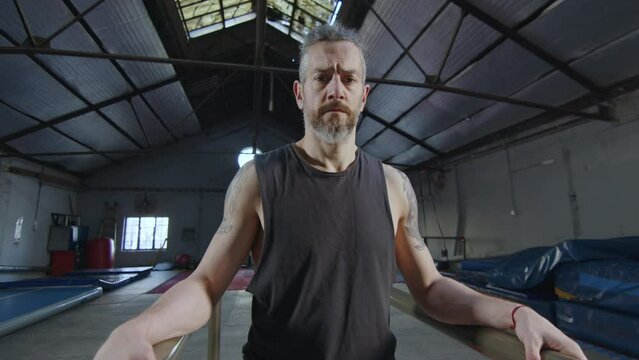 Confident sportsman standing between parallel bars and looking at camera in large training gym. Zoom shot, video portrait