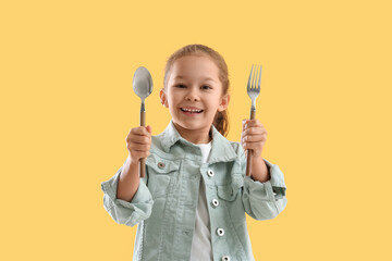 Cute little girl with fork and spoon on yellow background