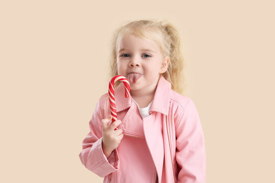 Cute little girl with candy cane on beige background