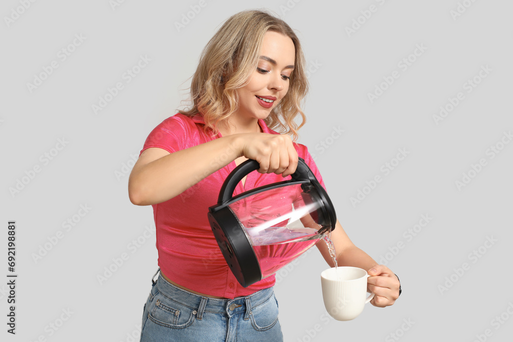 Wall mural Beautiful young woman pouring hot water from modern electric kettle into cup on white background