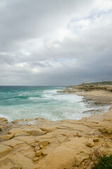 Fototapeta na wymiar Rocky shore against a cloudy sky and waves in the sea. Malta