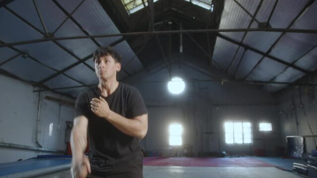 Young muscular athlete in sportswear doing alternate kettlebell overhead press during weightlifting workout in training gym
