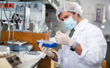 Middle-aged Latin male scientist researcher holding tripod and looking at reaction in test tube while performing biochemical tests in lab