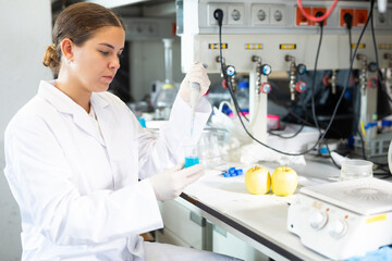 Young woman lab technician working in food testing laboratory, testing apple on pesticides and...