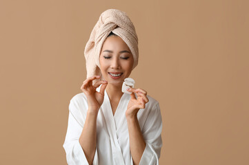 Young Asian woman in bathrobe with dental floss after shower on brown background