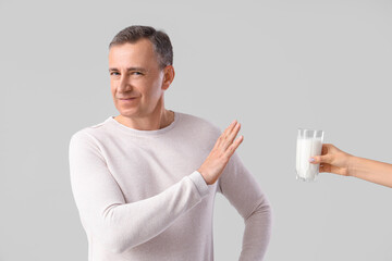 Mature man rejecting glass of milk on light background