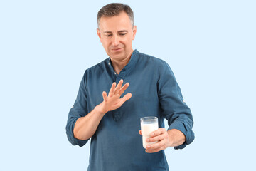 Displeased mature man rejecting glass of milk on blue background