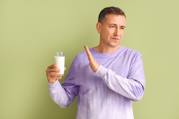 Mature man rejecting glass of milk on green background