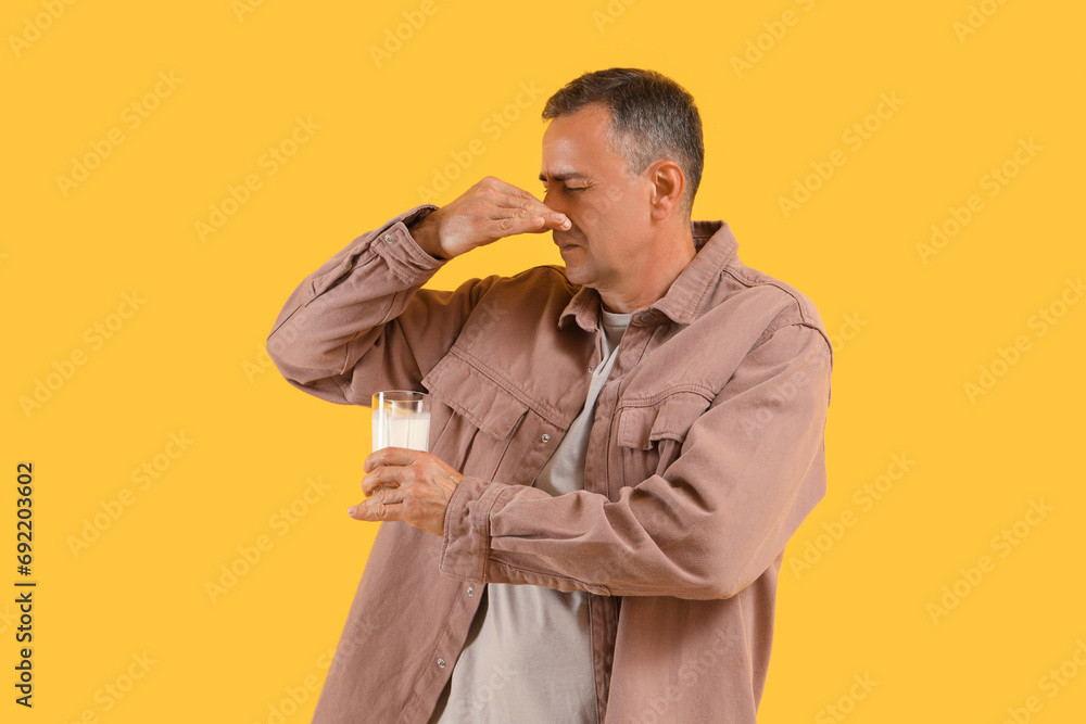 Canvas Prints Mature man with glass of milk covering nose on yellow background