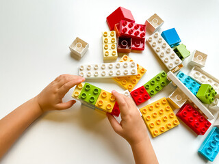 Child playing with colorful building blocks on white background. Top view