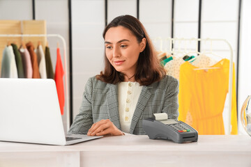 Female seller working with laptop at counter in clothing shop