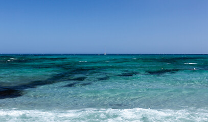 Clear blue water of Mediterranean sea and white sailboat anchored on horizon. Sardinia island, Italy on sunny day.