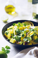 Healthy salad with avocado, mango, red onion and green coriander on a black plate with lime and olive oil.