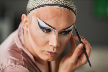Close up portrait of male drag performer doing makeup in dressing room, copy space