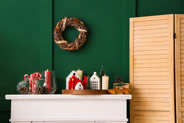 White mantelpiece with Christmas decorations and burning candles near green wall