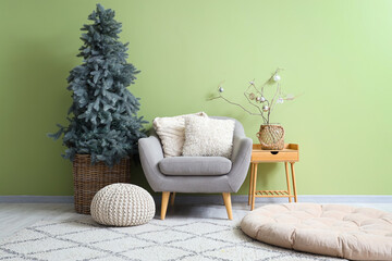 Interior of festive living room with Christmas tree, grey armchair and pouf near green wall