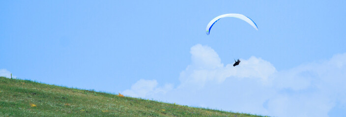 Paragliding sportsman flying high over a green field with a parachute