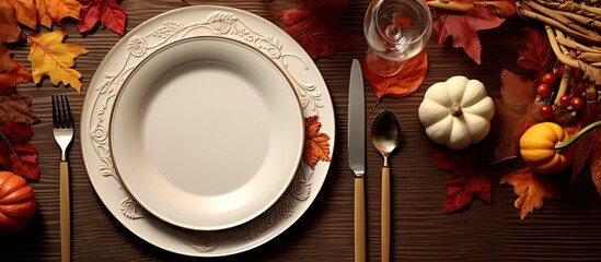 Autumn fall or thanksgiving table setting design captured from above top view flat lay White plate glass cutlery and decorations colorful leaves Dark moody light. Copy space image