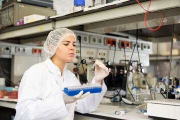 Focused young female lab technician working in research laboratory, conducting experiment, looking...