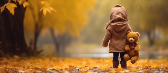 Fototapeta na wymiar Beautiful girl in yellow cloak holds teddy bear walking through autumn nature Young woman with soft toy outdoors. Copy space image. Place for adding text or design