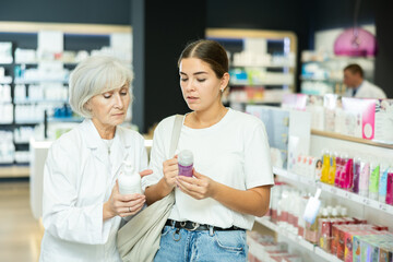 Thoughtful young girl choosing lubricant with help of mature female pharmacist in chemist's shop