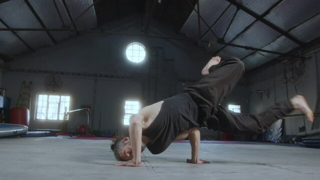 Professional male gymnast showing acrobatic performance on camera in a large training gym. He doing acro dance with elements of breakdance