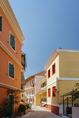 Fototapeta na wymiar A picturesque view of a quiet, sunlit alley framed by colorful houses with shutters, in a Mediterranean village