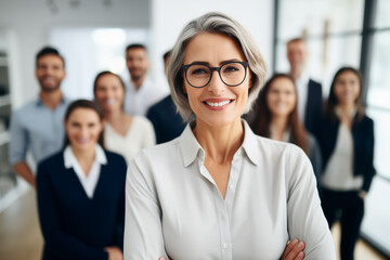 Fototapeta premium business woman wearing white jacket suit, in the office, her work team appears in the background out of focus. smiling woman. boss, businesswoman, leader