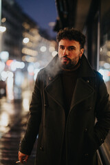 Fototapeta premium A stylish man smoking a cigarette while waiting for a taxi on a rainy night in the downtown area of a busy city.