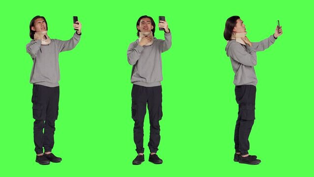 Guy having cervical neck brace makes phone call informing family about his vertebral fracture injury. Full body greenscreen of wounded man wearing medical foam collar, speaking on telephone.