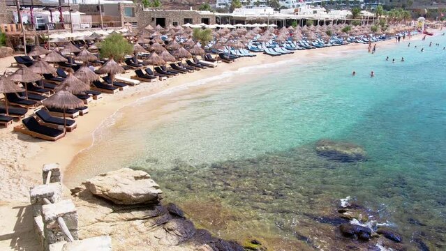 Paraside Beach in Mikonos, Greece, umbrella and luxury beach chairs beds in front of blue ocean. Most famous beach with crystal water and beach music bars. Gimbal cinematic ProRes graded from Log