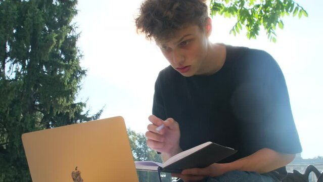 Adolescent student cross-references notes with information on laptop. Teenager incorporates contemporary technologies into study routine