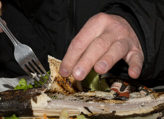 The process of eating fish in a restaurant. Butchering trout with a fork and hands. Close-up action.