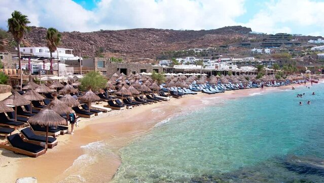 Paraside Beach in Mikonos, Greece, umbrella and luxury beach chairs beds in front of blue ocean. Most famous beach with crystal water and beach music bars. Gimbal cinematic ProRes graded from Log