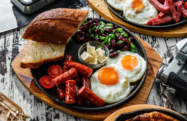 Delicious breakfast with fried eggs, slices of bread, sausage and salad of beans served on hot pan...