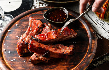 Hands cut barbecue pork spare ribs with hot honey chilli marinade on wooden cutting board with sauce on rustic background. Close up