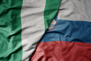 big waving national colorful flag of slovenia and national flag of nigeria .