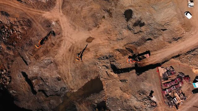 Aerial drone footage of large excavation site with lots of heavy industry vehicles filmed from above. View of construction place and machinery digging and loading ground in bulldozers. Building roads.