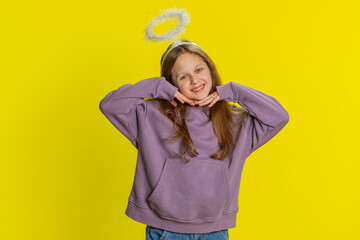Portrait of smiling shy angelic young preteen child girl kid with angel halo nimb over head flirting, looking at camera, positive emotions, celebrating holiday. Children isolated on yellow background - obrazy, fototapety, plakaty