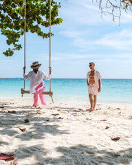 A couple of men and women at a swing on the beach of Koh Samet Island Thailand, tropical beach on Samed Island with a turqouse colored ocean. Asian women and European men on vacation in Thailand