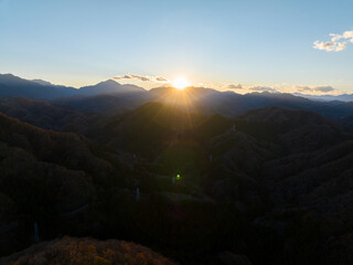 遠くの山に沈む夕日と夕日に照らされた紅葉した山々　空撮
